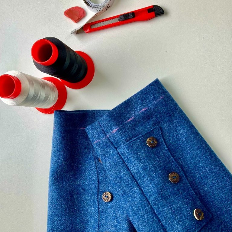 Kilt jacket alteration Greenock Blue kilt jacket with buttons, thread spools, and a craft knife on a surface.