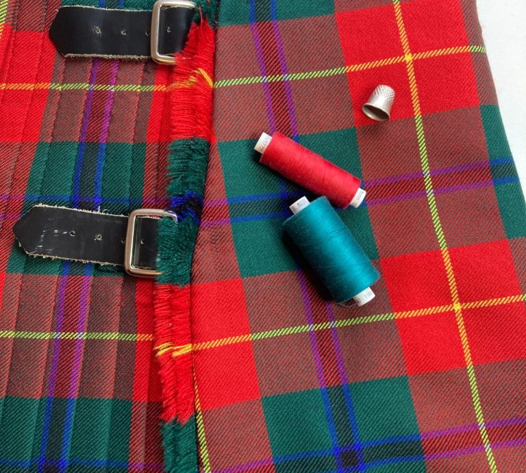 Kilt alteration and repair specialists Ayr Tartan fabric with sewing threads in red, teal, and a metal thimble.